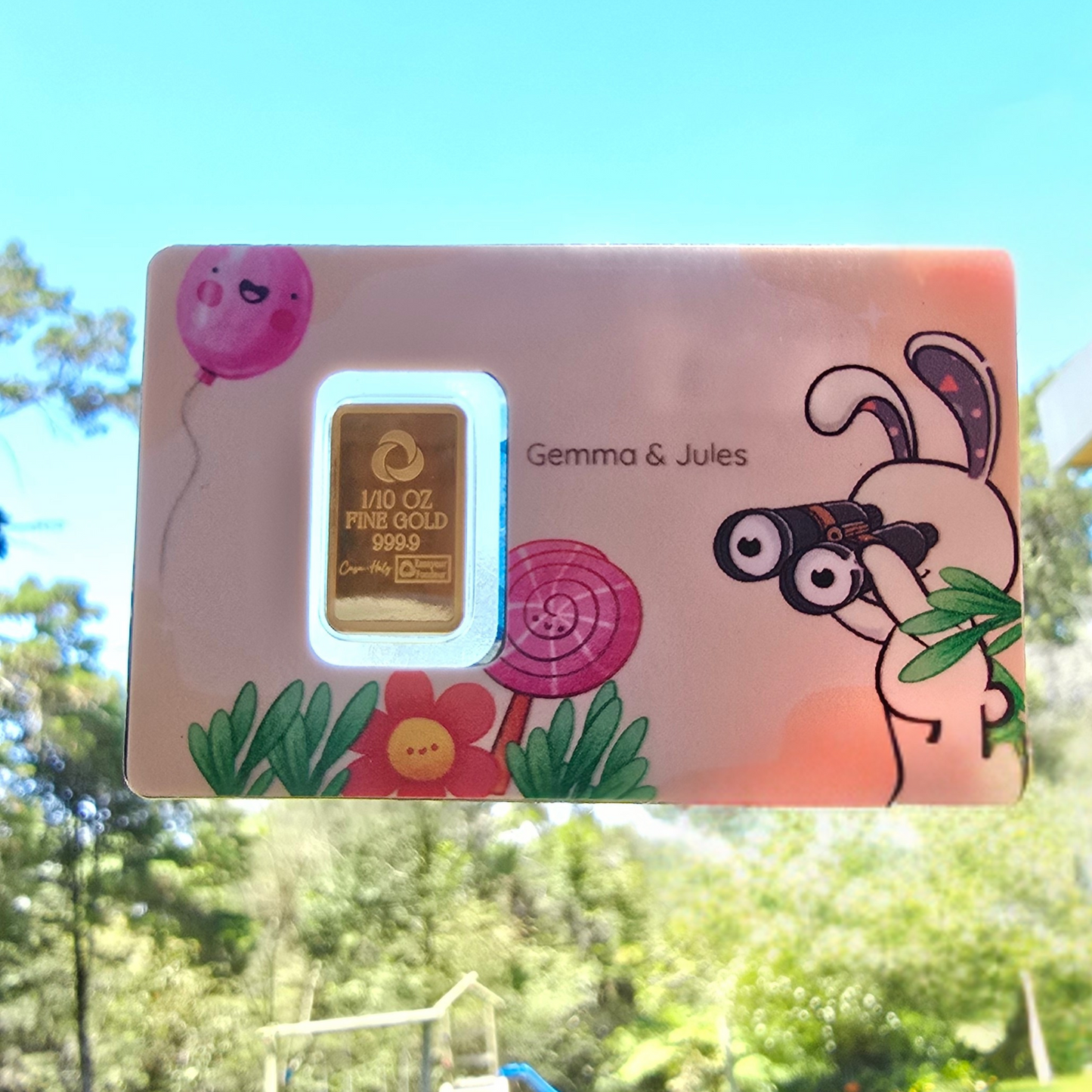 Gold bar in a colorful box with cartoon characters and 'Gemma & Jules' branding, outdoors.