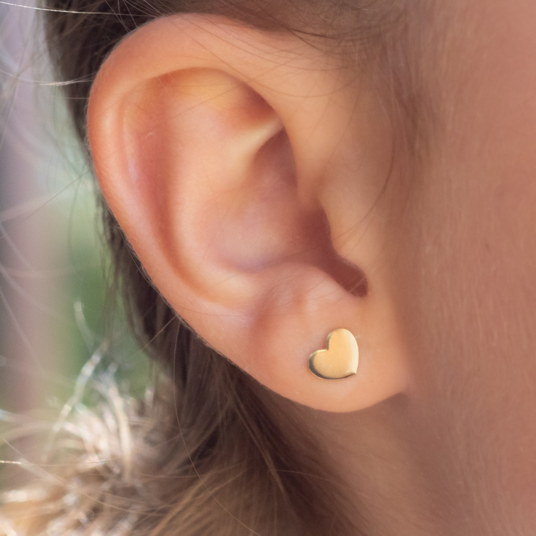 Close-up of an ear wearing a gold heart-shaped earring with a blurred background